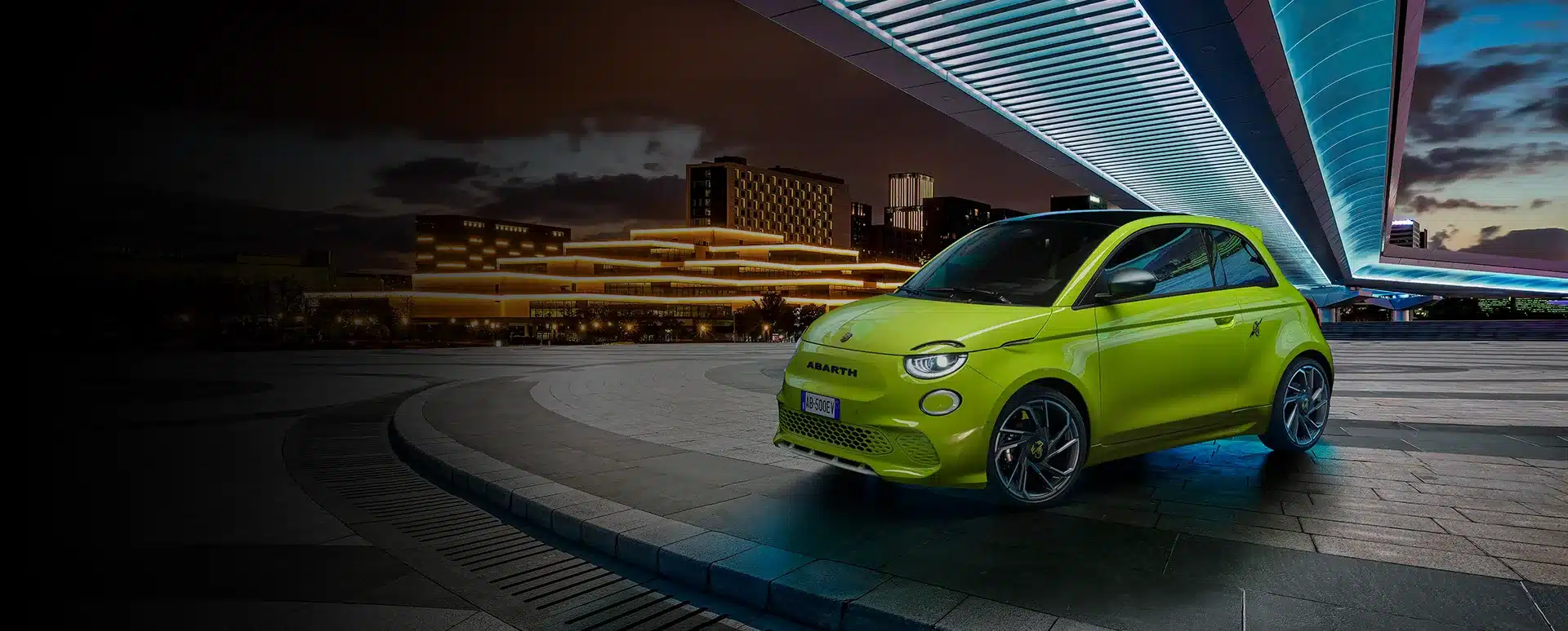 Abarth 500e in leuchtend gelber Lackierung vor beleuchteter moderner Architektur bei Nacht