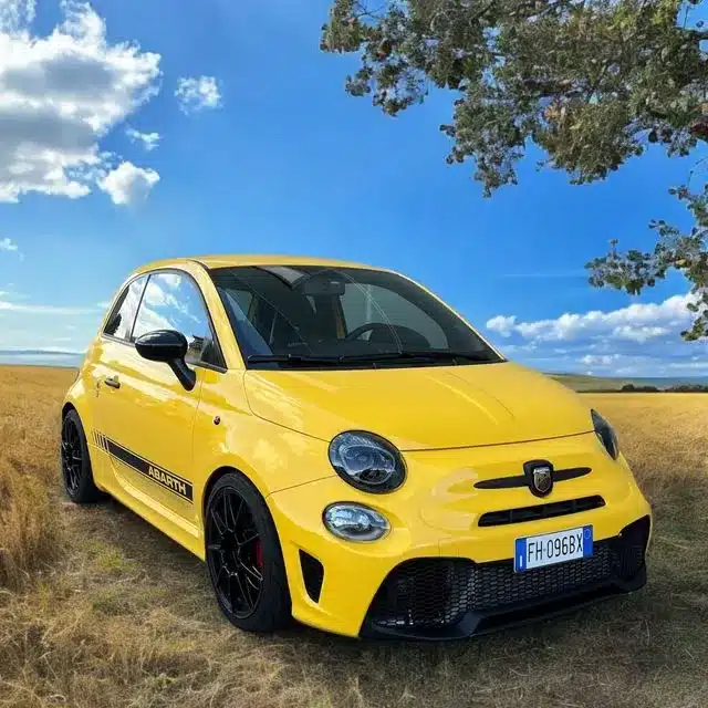 Gelber Abarth 595 mit schwarzer Akzentuierung steht auf einem Feldweg unter blauem Himmel.