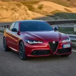 Rote Alfa Romeo Giulia fährt auf einer kurvigen Landstraße in bergiger Landschaft.