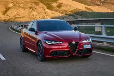 Rote Alfa Romeo Giulia fährt auf einer kurvigen Landstraße in bergiger Landschaft.