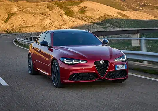 Rote Alfa Romeo Giulia fährt auf einer kurvigen Landstraße in bergiger Landschaft.