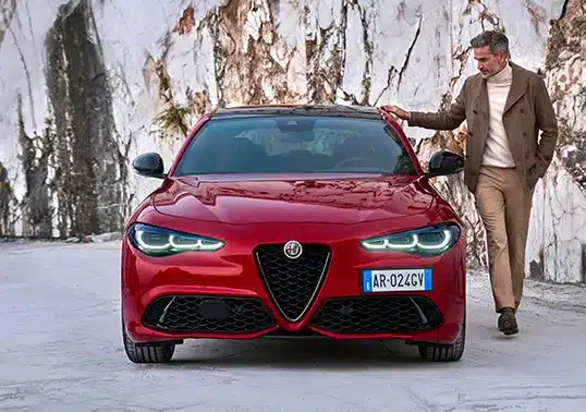 Frontansicht einer roten Alfa Romeo Giulia mit Fahrer vor einer Marmorkulisse.