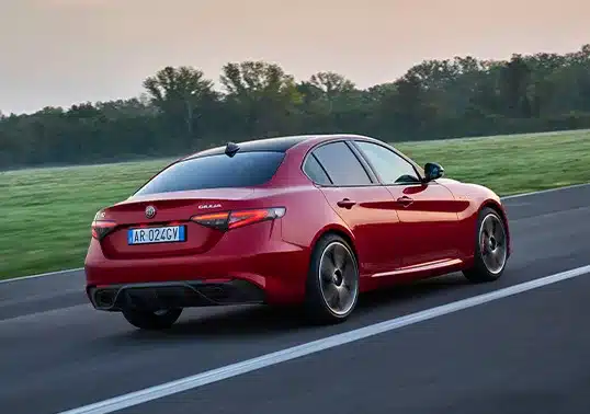 Heckansicht einer roten Alfa Romeo Giulia Limousine auf einer Landstraße bei Sonnenuntergang