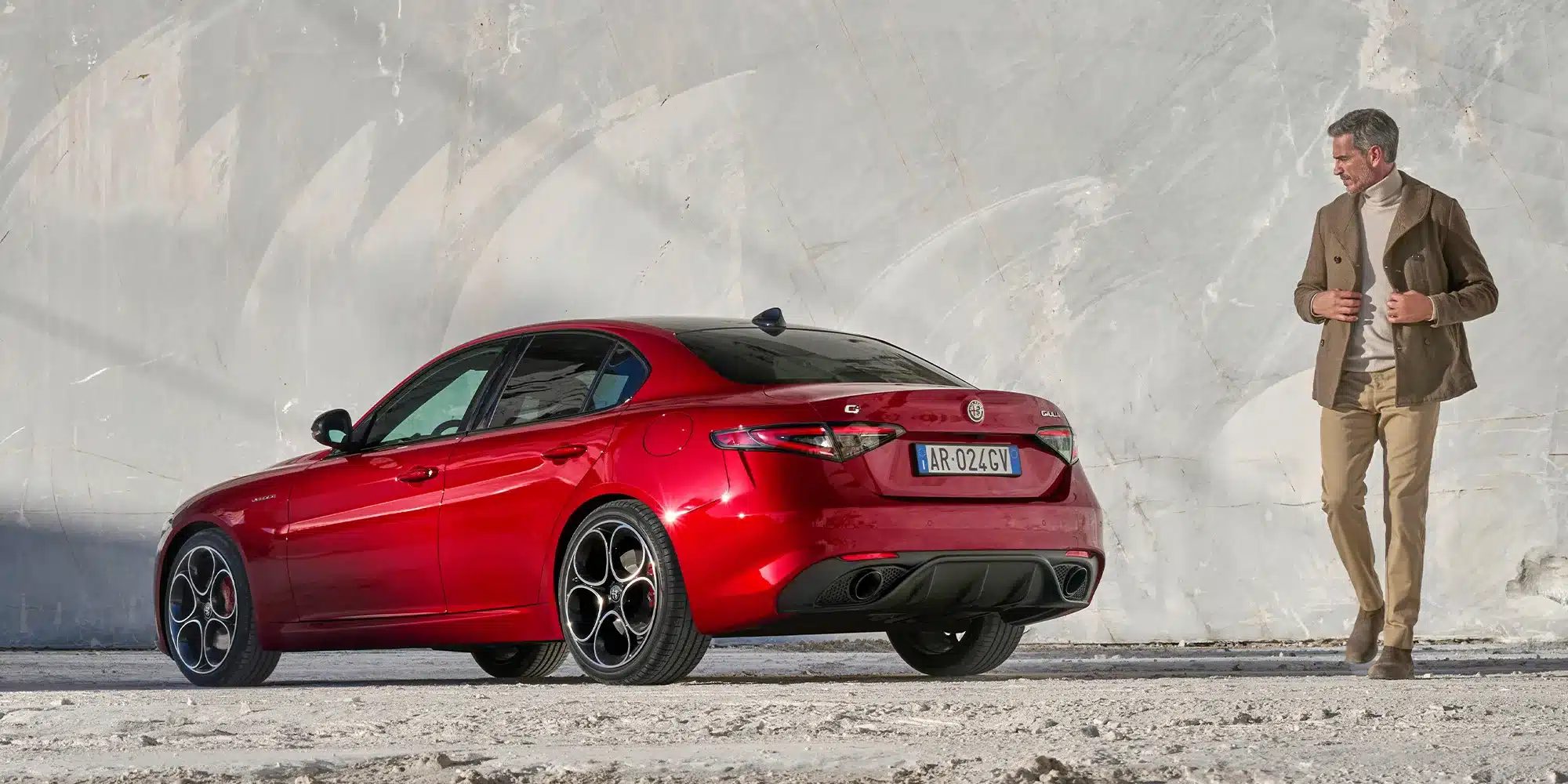 Rote Alfa Romeo Giulia Limousine seitlich und von hinten, daneben ein Mann vor heller Wand.