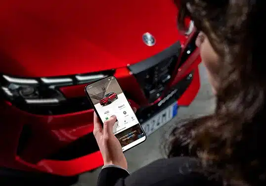 Frau hält ein Smartphone mit Alfa Romeo Junior Elettrica App vor dem roten Fahrzeug