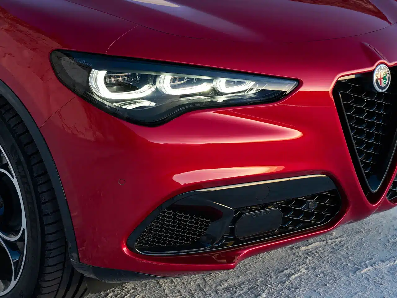Nahaufnahme des LED-Frontscheinwerfers und Alfa Romeo Marken-Kühlergrills am roten Stelvio SUV
