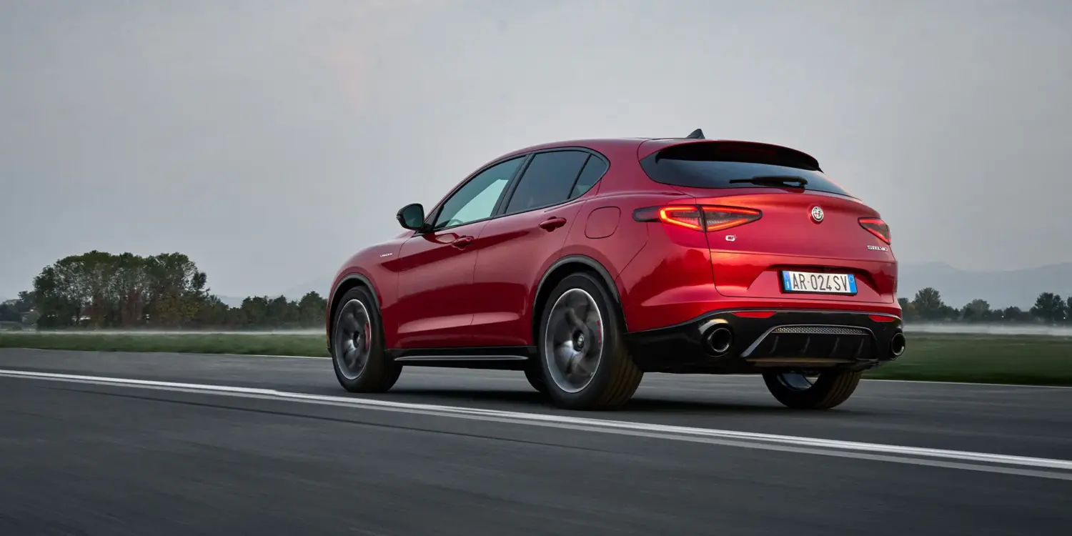 Roter Alfa Romeo Stelvio fährt auf einer Landstraße, Sport-SUV von hinten fotografiert.