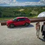Roter Alfa Romeo Tonale SUV am Aussichtspunkt mit zwei Personen im Vordergrund und Weinbergen im Hintergrund
