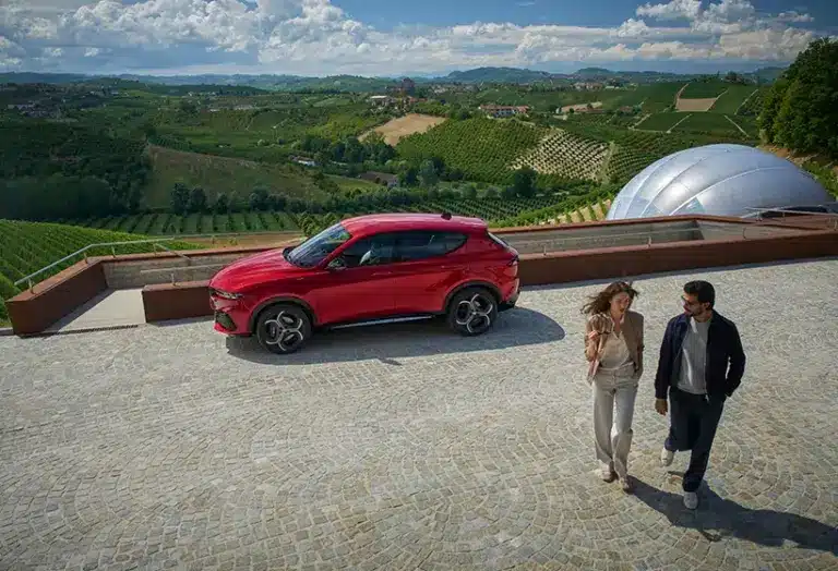 Roter Alfa Romeo Tonale SUV am Aussichtspunkt mit zwei Personen im Vordergrund und Weinbergen im Hintergrund