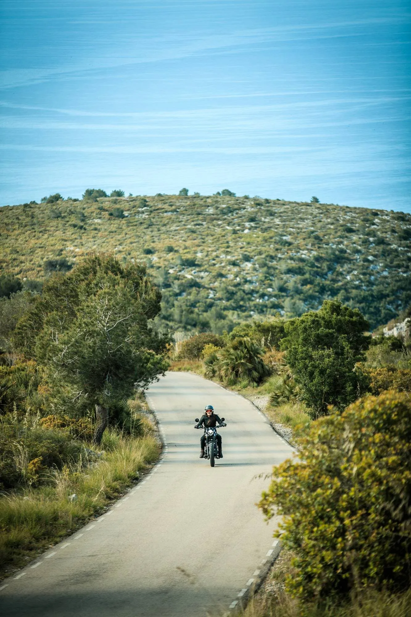 Motorradfahrer auf einer Brixton Cromwell 125 fährt auf ruhiger Landstraße durch hügelige Landschaft