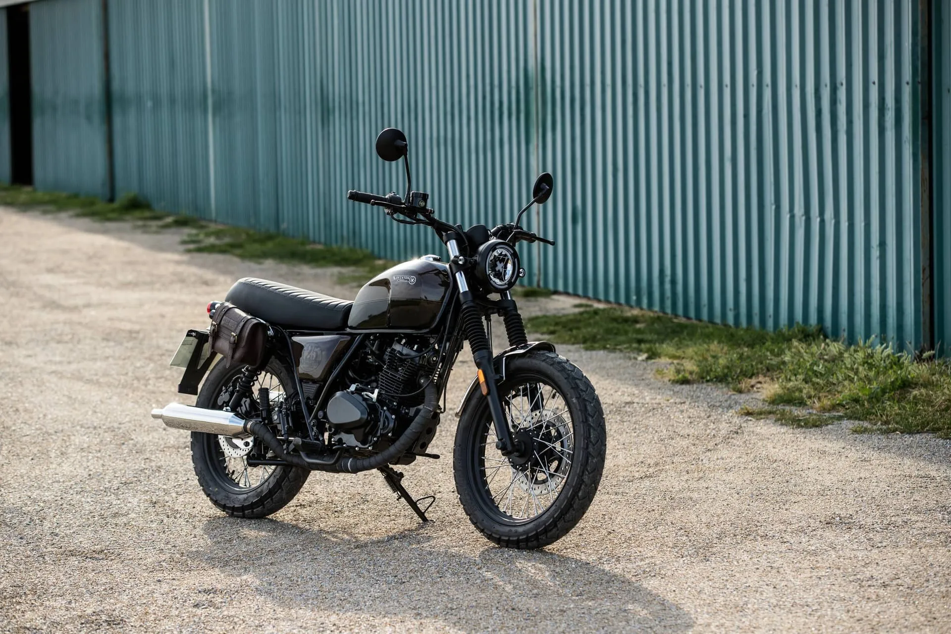 Brixton Cromwell 125 Motorrad steht auf einem Schotterweg vor einer grünen Blechhalle.
