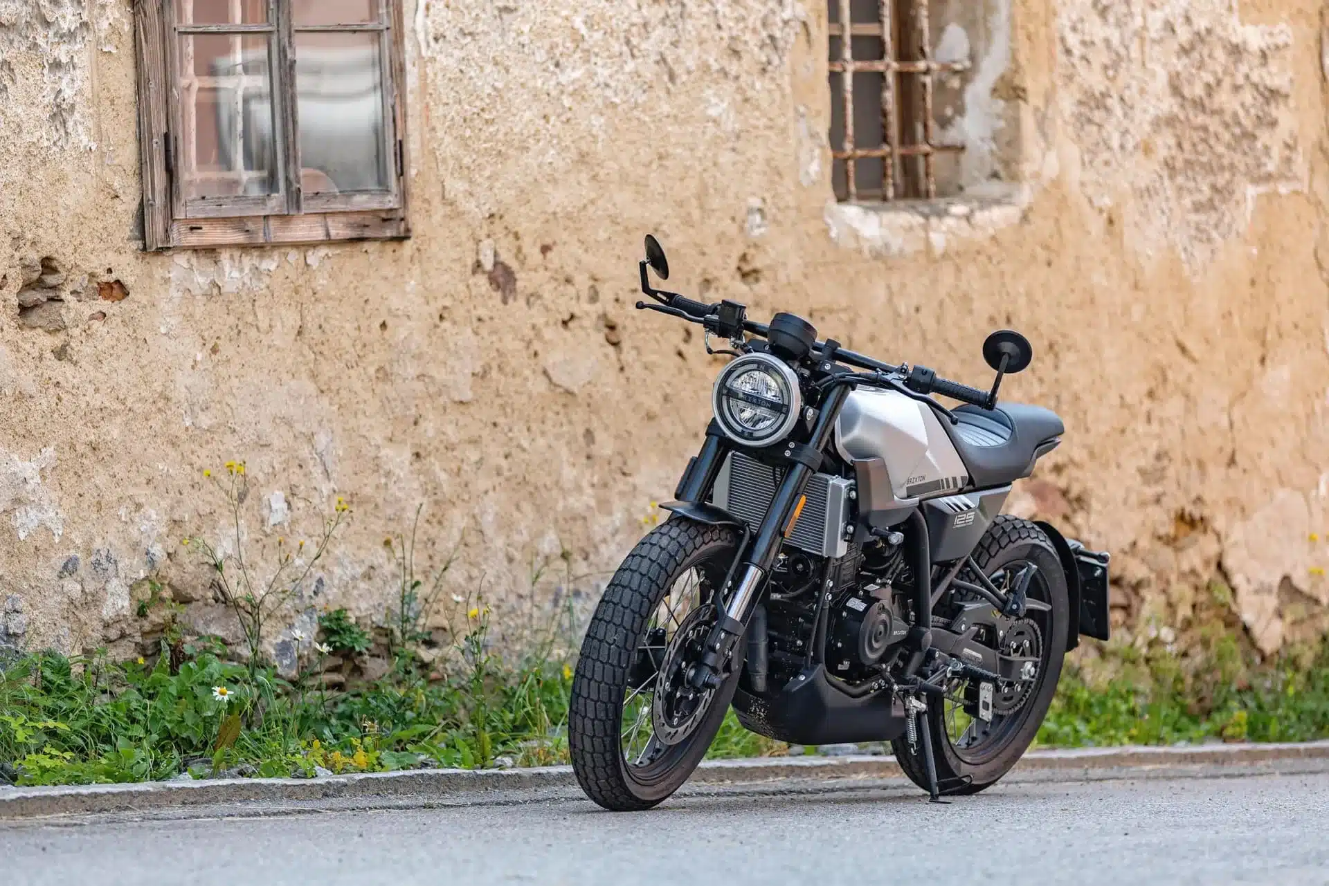 Silberne Brixton Crossfire 125 Motorrad, geparkt vor einer alten Wand mit Fenstern.