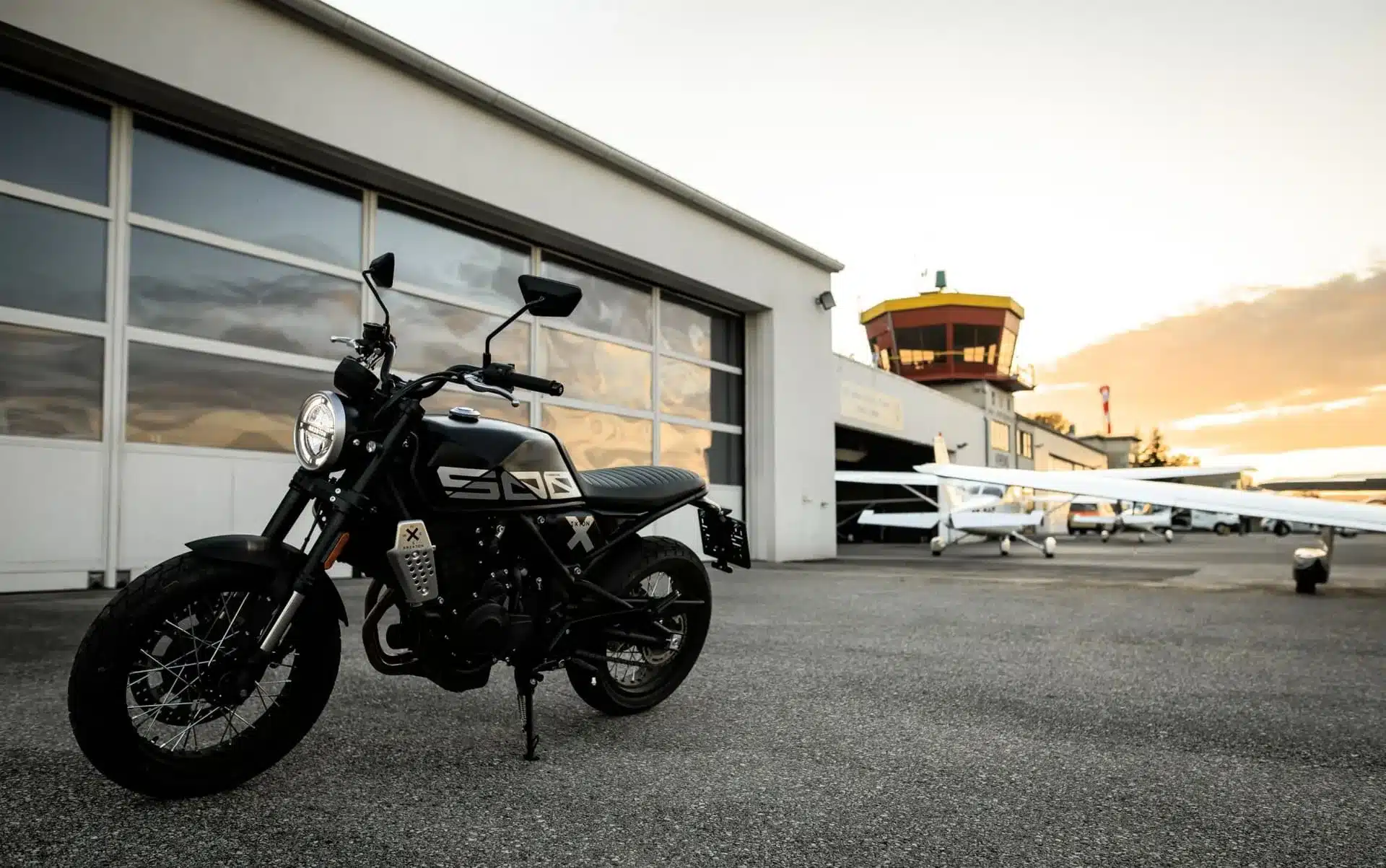 Brixton Crossfire 500 X Motorrad steht vor Flugzeug-Hangar bei Sonnenuntergang
