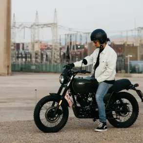 Person sitzt auf einer Brixton Felsberg 125 vor Industriegebäuden im Freien