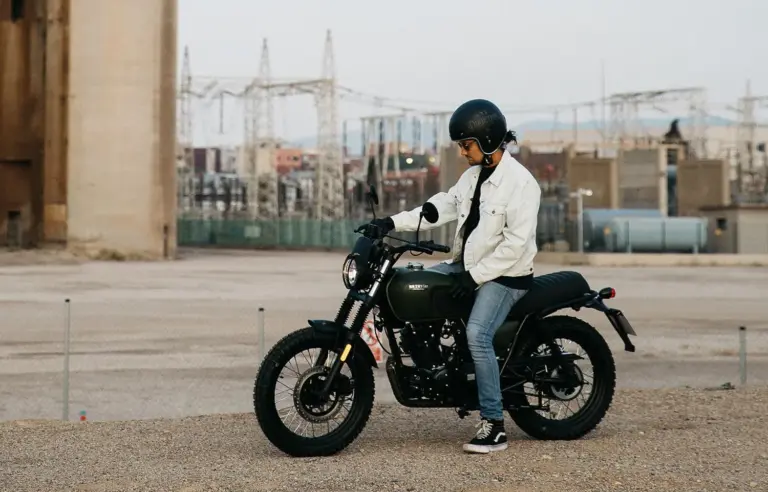 Person sitzt auf einer Brixton Felsberg 125 vor Industriegebäuden im Freien