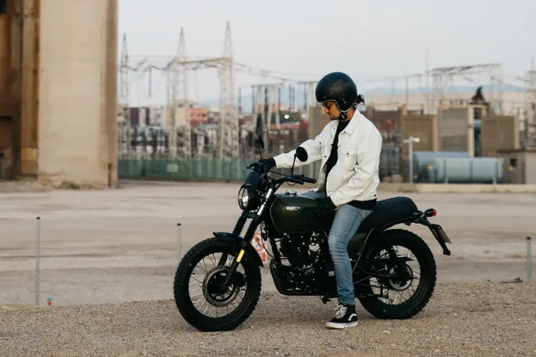 Person sitzt auf einer Brixton Felsberg 125 vor Industriegebäuden im Freien