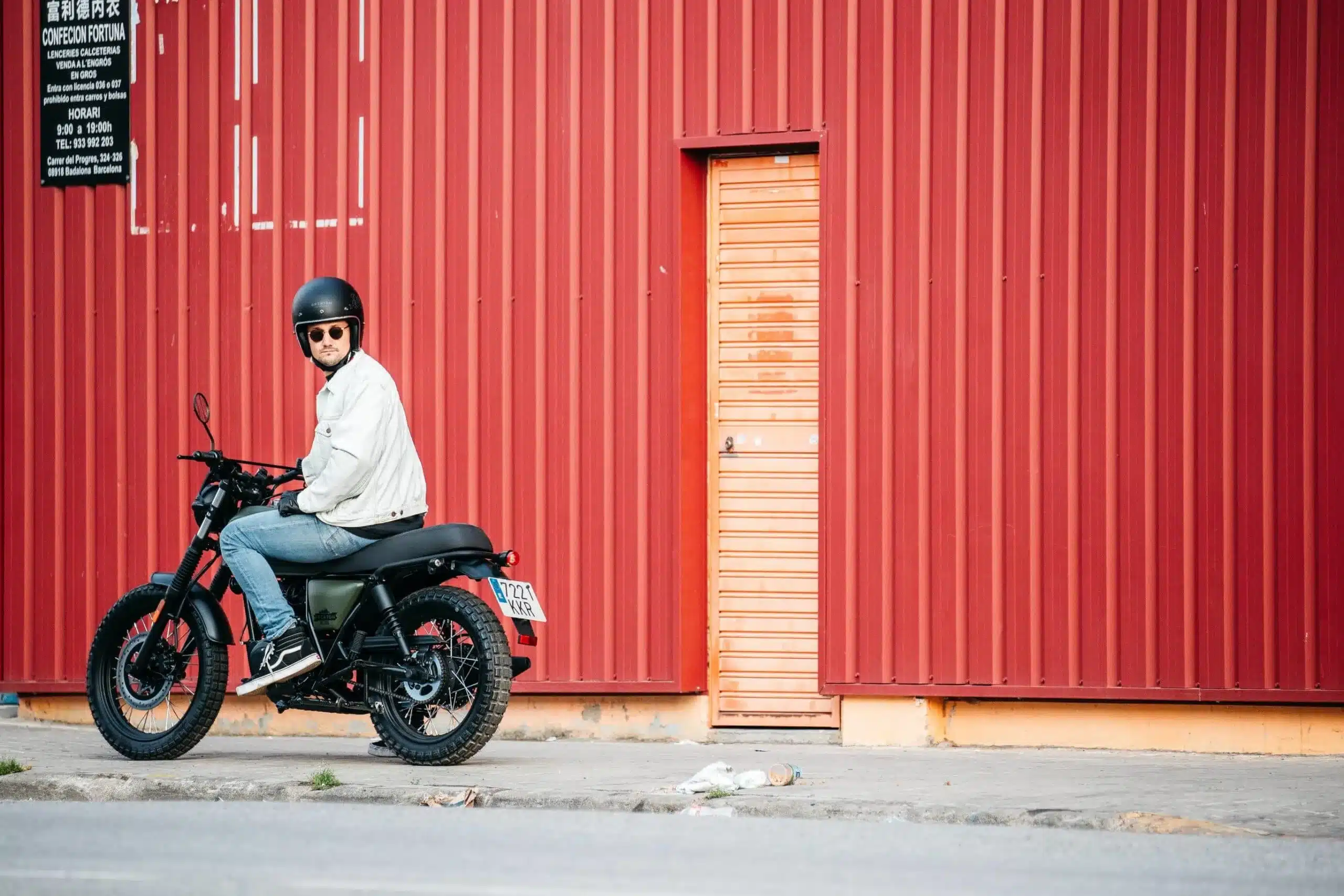 Mann sitzt auf einer Brixton Felsberg 125 Scrambler vor einer rot gestrichenen Industriehalle