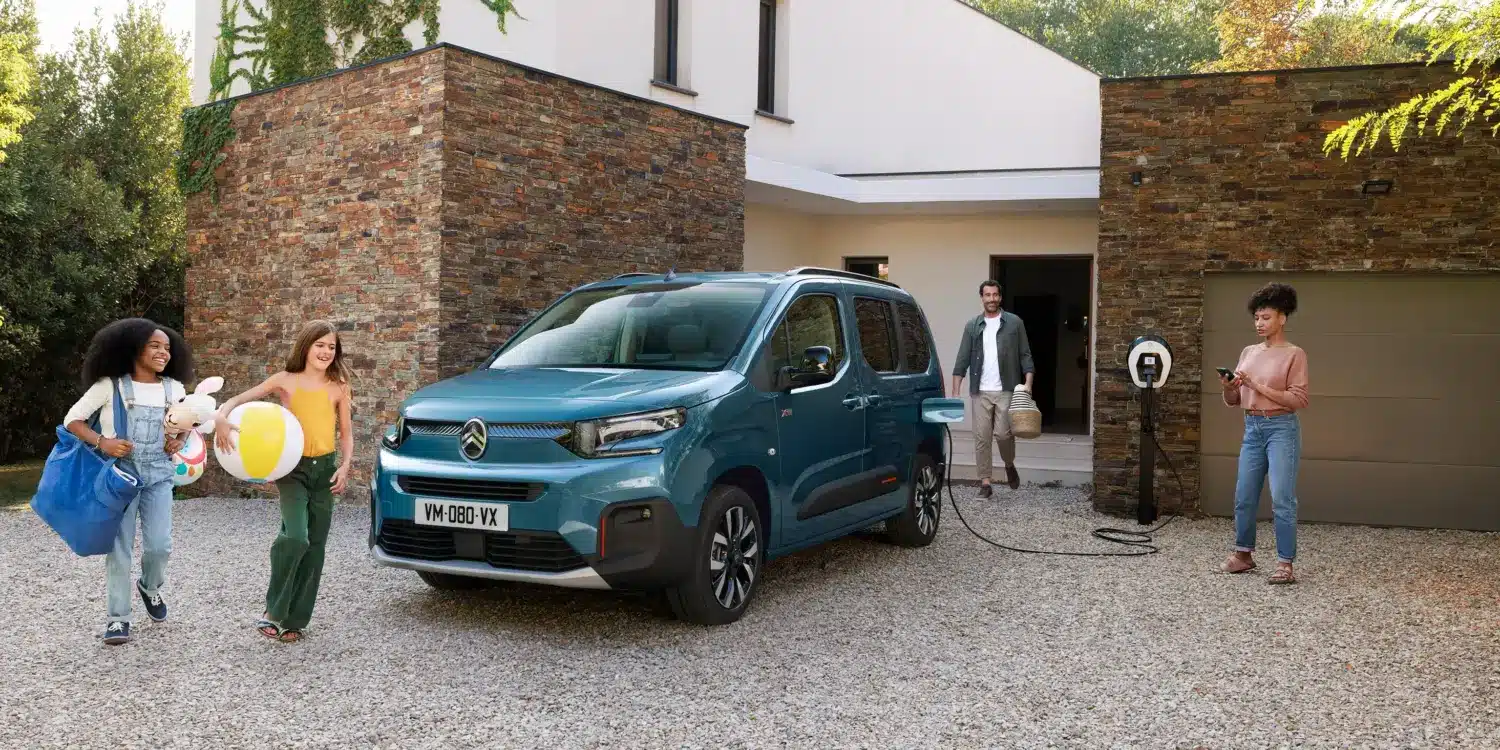Citroën ë-Berlingo wird an einer Wallbox vor einem modernen Haus geladen, Familie im Vordergrund.