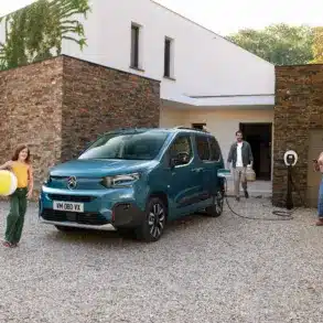 Citroën ë-Berlingo wird an einer Wallbox vor einem modernen Haus geladen, Familie im Vordergrund.