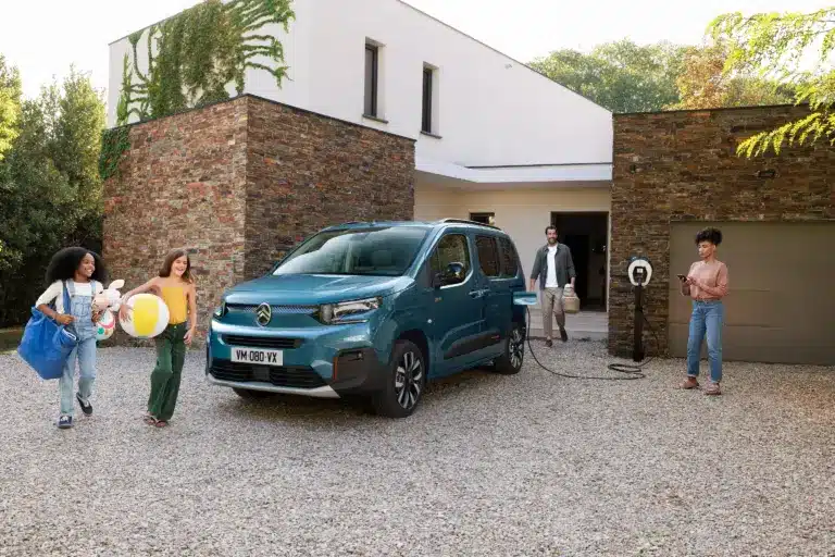 Citroën ë-Berlingo wird an einer Wallbox vor einem modernen Haus geladen, Familie im Vordergrund.