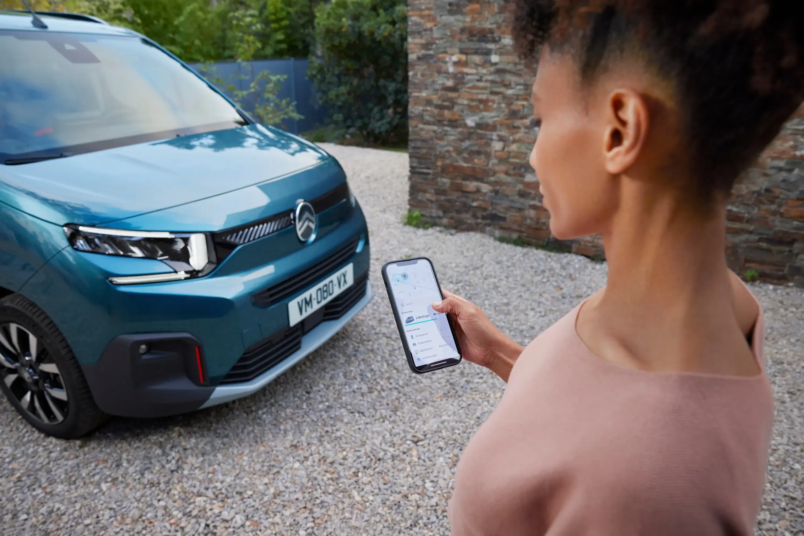 Frau steht vor einem Citroën ë-Berlingo und nutzt ein Smartphone zur Steuerung des Ladevorgangs.