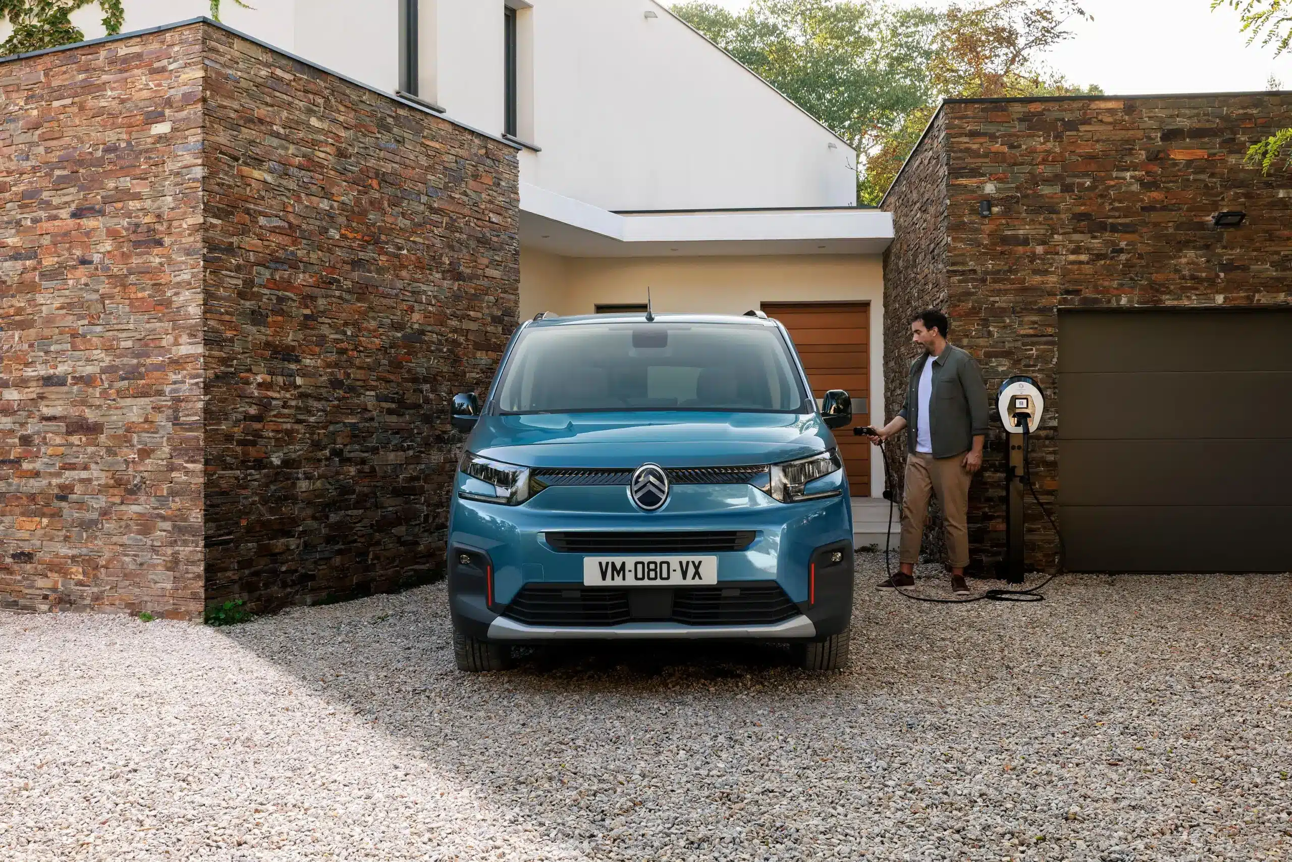 Citroën ë-Berlingo in blau, stehend vor einem modernen Haus und verbunden mit einer Wallbox.