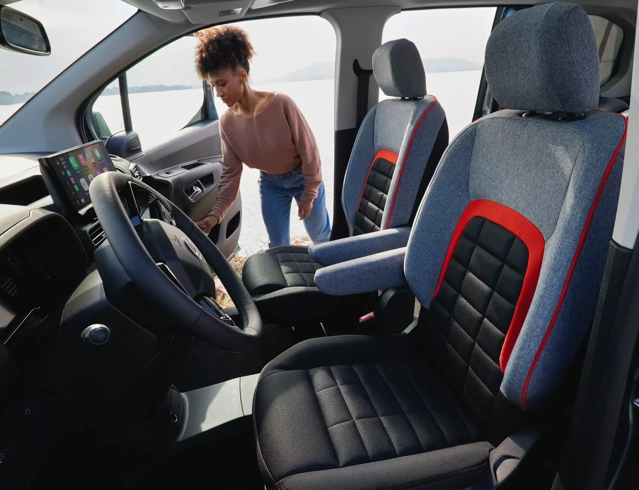 Innenraum des Citroën ë-Berlingo mit modernem Cockpit, Polstersitzen und Frau am Fahrzeug.