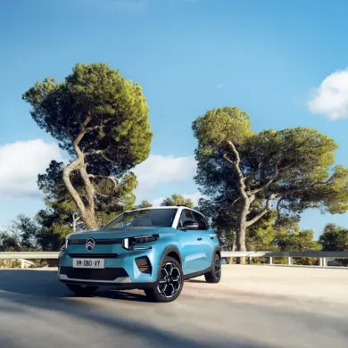 Citroën ë-C3 in blauer Lackierung auf einem Parkplatz, Bäume im Hintergrund, strahlender Himmel.