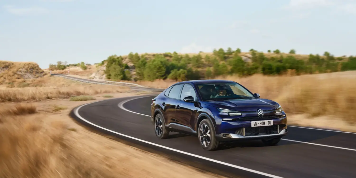 Citroën New C4 X in blau fährt auf einer kurvigen Landstraße durch hügelige Landschaft.