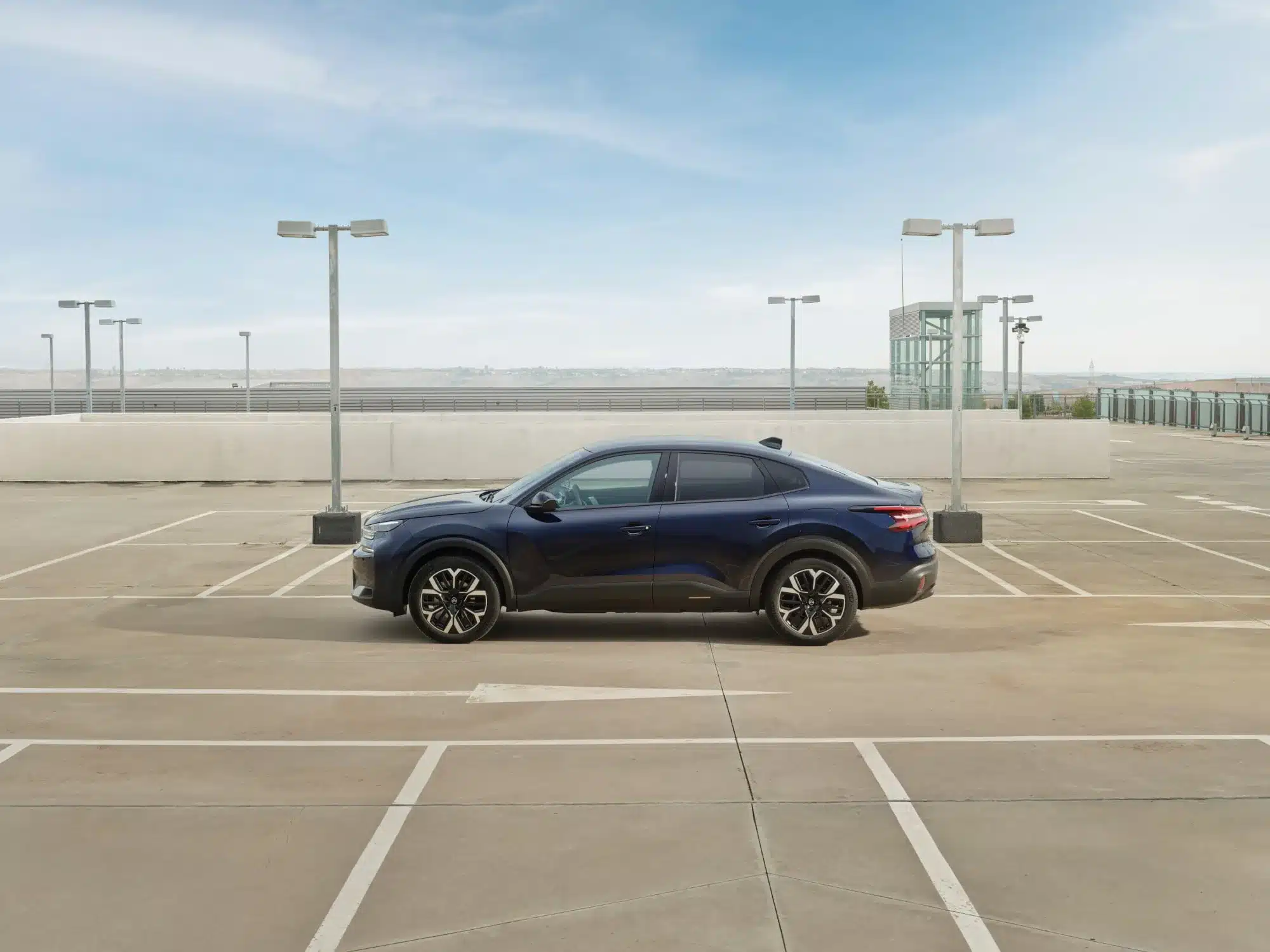 Seitenansicht eines blauen Citroën New C4 X auf einem leeren Parkdeck unter blauem Himmel.