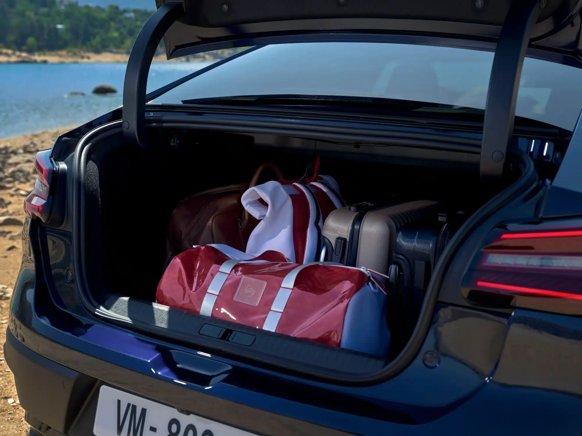 Kofferraum des Citroën New C4 X mit mehreren Taschen und Koffern am Ufer eines Sees.