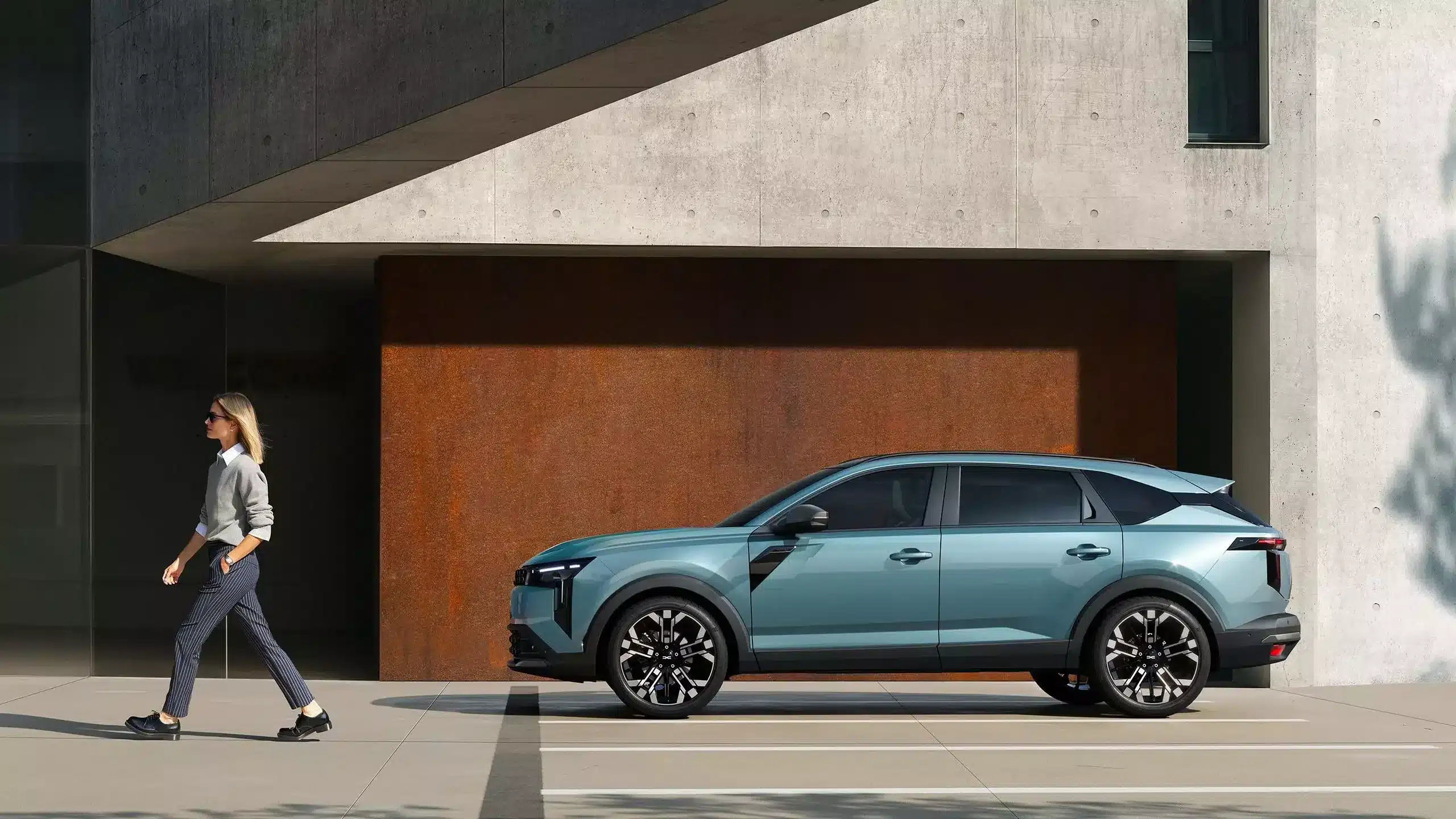 Dacia Striker Hybrid-Crossover in blau, Seitenansicht, vor einer Betonwand geparkt