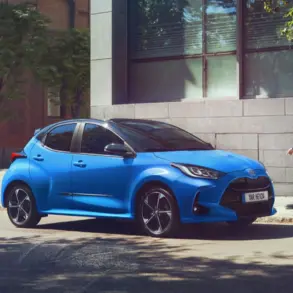 Blauer Toyota Yaris Hybrid geparkt am Straßenrand vor einem modernen Gebäude, eine Frau geht auf dem Gehweg vorbei.