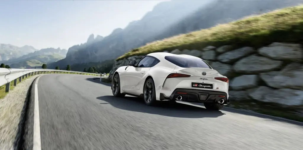 Toyota GR Supra 2025 fährt sportlich durch eine Berglandschaft, Heckansicht auf der Straße.