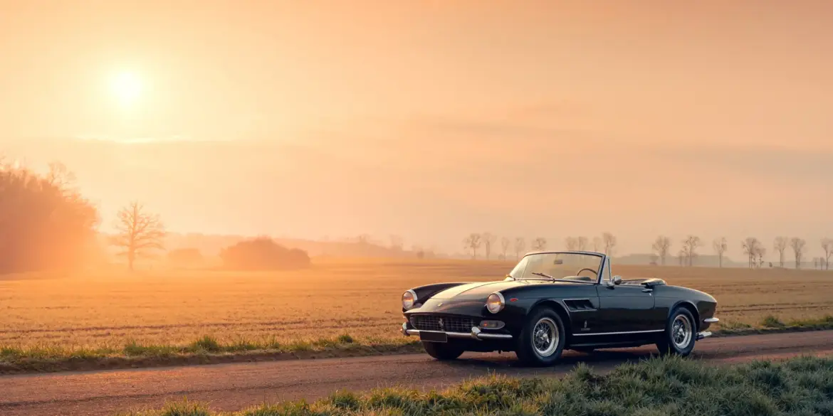 Ferrari 275 GTS Cabriolet, Baujahr 1965, schwarz, auf einer Landstraße bei Sonnenaufgang, ländliche Kulisse.