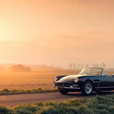 Ferrari 275 GTS Cabriolet, Baujahr 1965, schwarz, auf einer Landstraße bei Sonnenaufgang, ländliche Kulisse.
