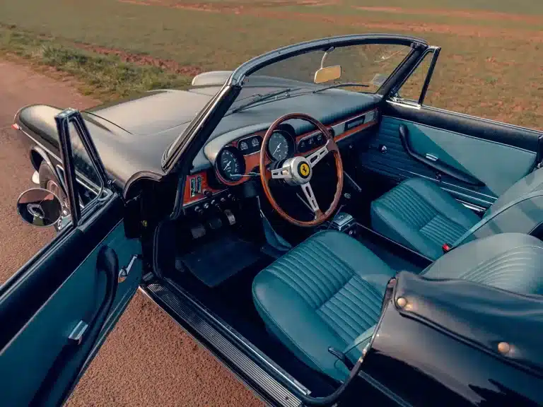 Innenansicht des Ferrari 275 GTS, klassisches Cockpit mit blauem Leder, offen, auf einer Landstraße stehend.