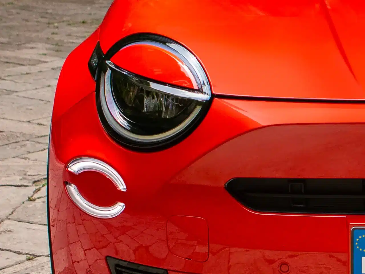 Nahaufnahme vom linken Frontscheinwerfer eines roten Fiat 600 Elektro mit markentypischen LED-Details