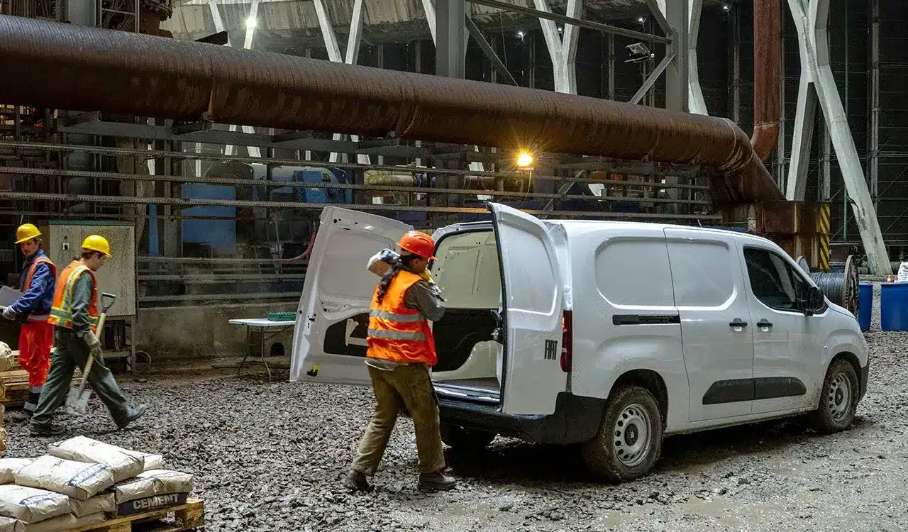 Fiat Doblò 25th Anniversary als Kastenwagen auf einer Baustelle mit offenem Laderaum und Arbeiter mit Baumaterial.