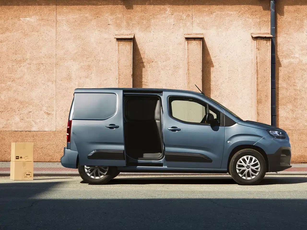 Fiat Doblò 25th Anniversary mit geöffneter Seitentür und Kartons auf der Straße vor einer Hauswand.