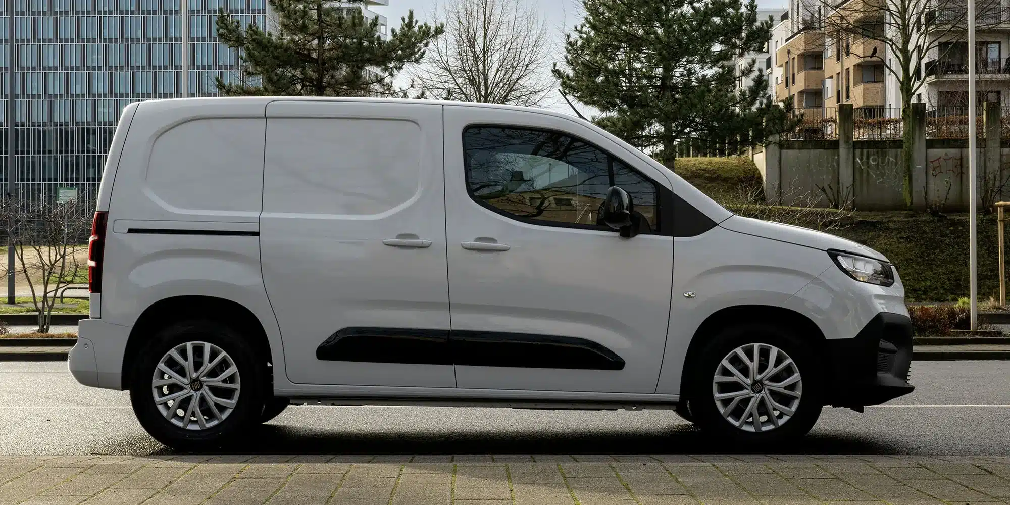 Fiat Doblò 25th Anniversary in weiß, Seitenansicht, auf städtischer Straße geparkt.