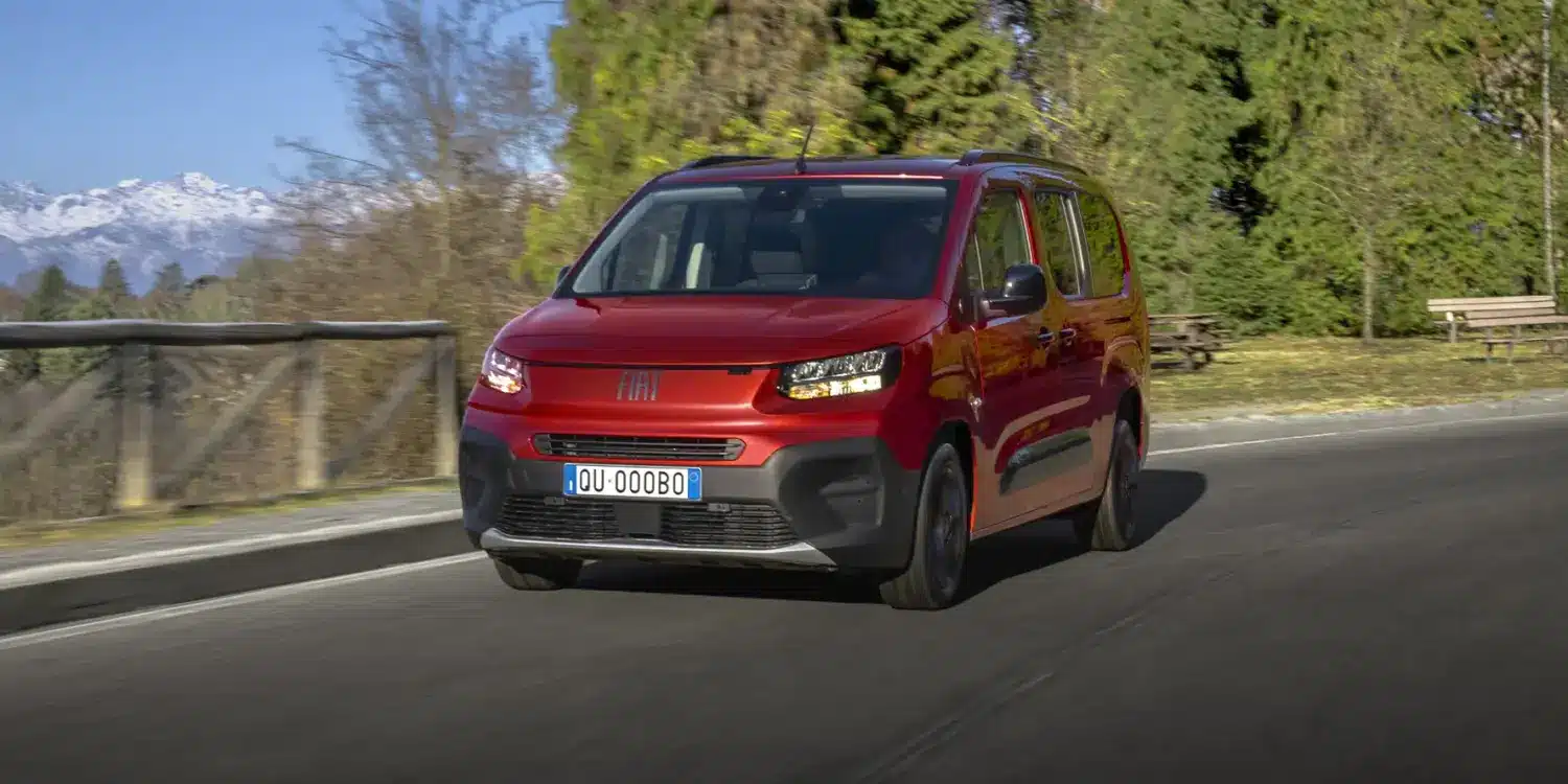 Roter Fiat Qubo L fährt auf einer Straße mit Bergen im Hintergrund.