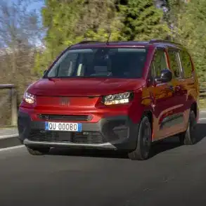Roter Fiat Qubo L fährt auf einer Straße mit Bergen im Hintergrund.