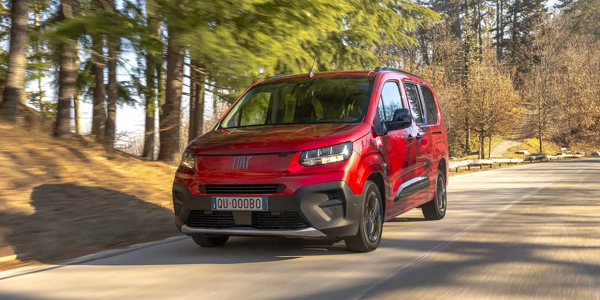 Roter Fiat Qubo L (RED) Edition auf einer Landstraße zwischen Bäumen, Frontansicht, fahrend.