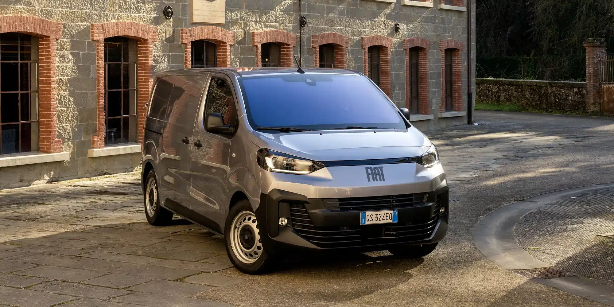 Neuer Fiat Scudo Transporter in Silber, geparkt vor einem Ziegelgebäude.