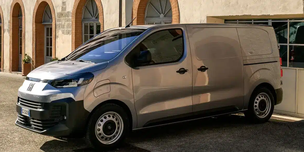 Fiat Scudo Transporter, Modelljahr 2024, geparkt vor einem historischen Gebäude mit Rundbogenfenstern.