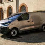 Fiat Scudo Transporter, Modelljahr 2024, geparkt vor einem historischen Gebäude mit Rundbogenfenstern.