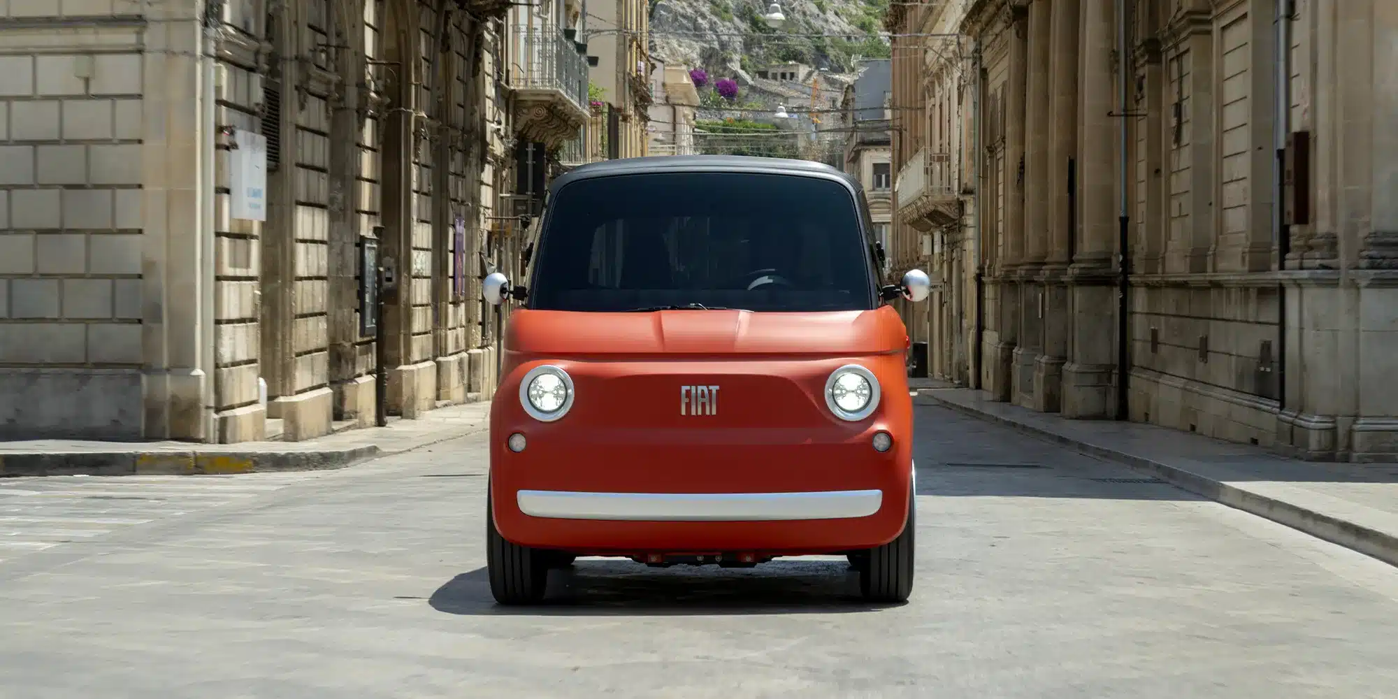 Fiat Topolino Microcar elektrisch, orange, frontal in einer Altstadtstraße