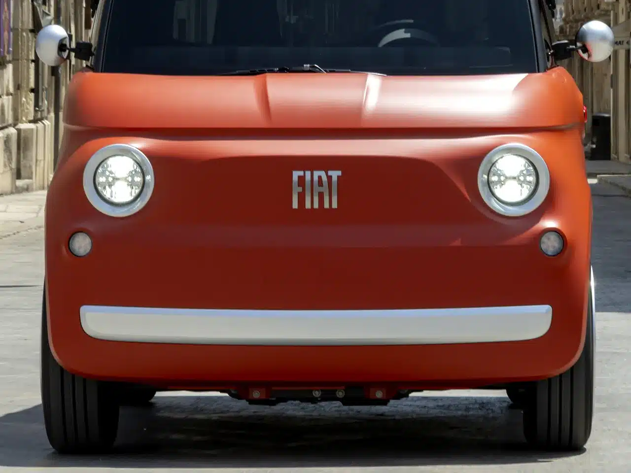 Frontansicht des elektrischen Microcars Fiat Topolino in der Farbe Corallo-Orange auf einer Stadtstraße.