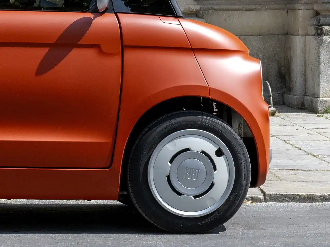 Detailaufnahme der vorderen linken Seite des Fiat Topolino Microcars in Corallo mit sichtbarem Reifen und Spiegel.